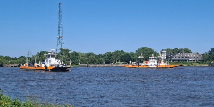 Zwei orangefarbene Fähren begegnen einander bei sonnigem Wetter auf dem Fluss.