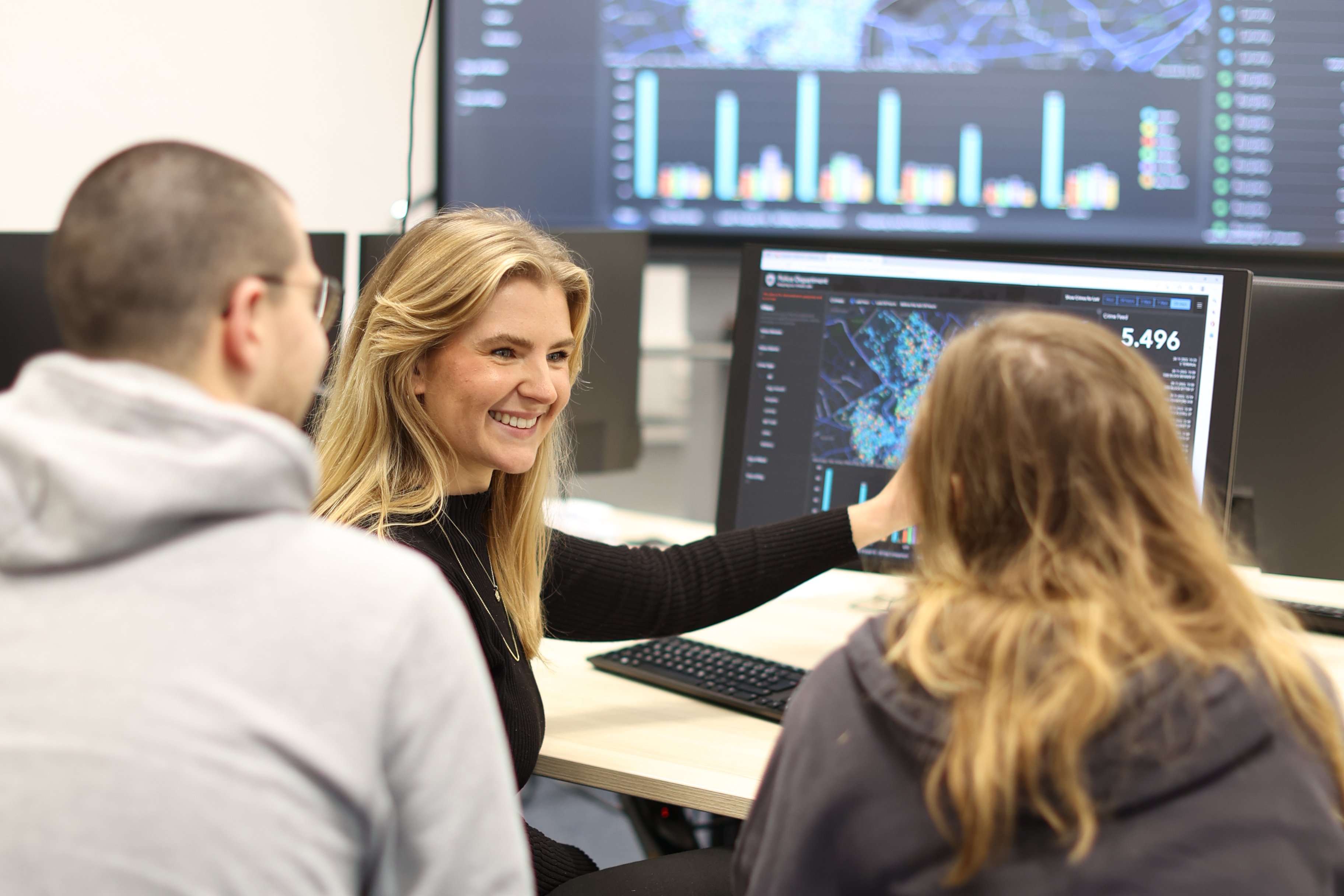 Studierende sitzen vor Bildschirmen und besprechen etwas.