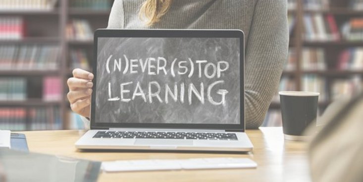 Das Bild zeigt eine Person, welche nicht mit dem Gesicht zu sehen ist, während sie einen aufgeklappten Laptop präsentiert, auf dessen Bildschirm "never stop learning" geschrieben steht.