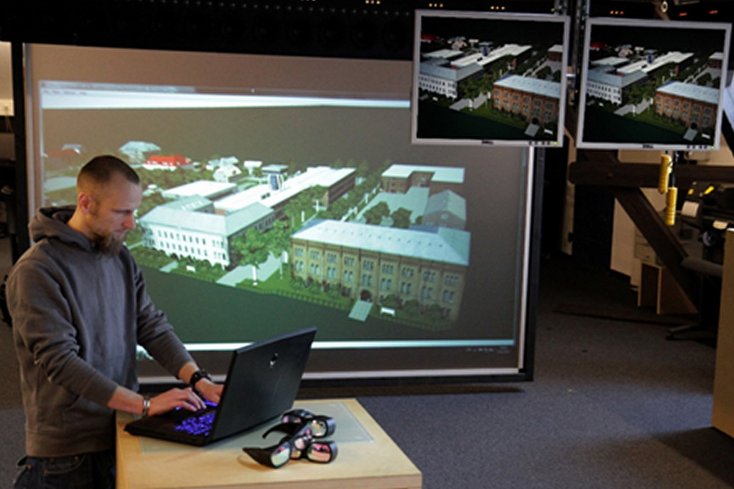 Herzstück des Labors für Virtuelle Welten der Jade Hochschule ist eine Projektionswand, auf der die Qualität von 3D-Modellen sichtbar wird. Im Bild: Tobias Theuerkauff, M. Sc., zu dieser Zeit Wissenschaftlicher Mitarbeiter im Labor für Virtuelle Welten, zeigt ein virtuelles Modell des Campus, das in verschiedenen Projekten entstanden ist. Foto: Jade Hochschule