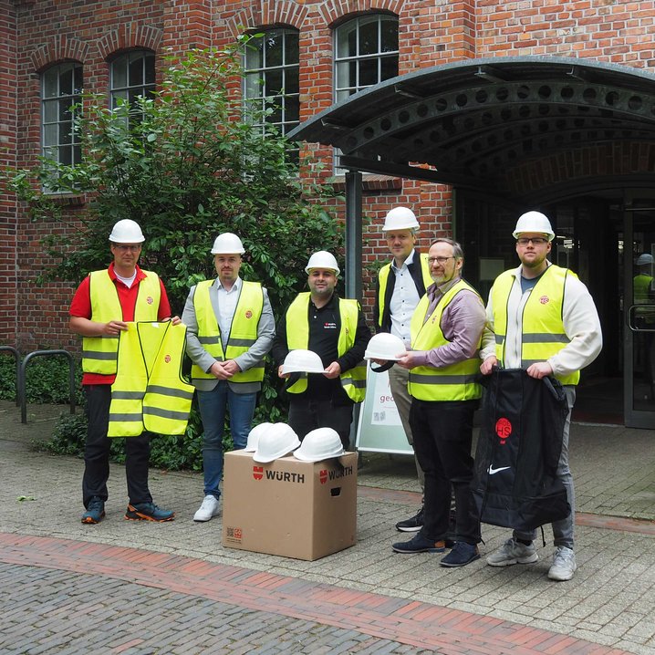 Prof. Dr. Sebastian Hollermann (IDoK/Jade HS (links)) sowie Firmenvertreter bei der Übergabe von Bauhelmen und Warnwesten (Foto: Jade HS)