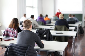 Studierende sitzen an Schreibtischen während einer Vorlesung.