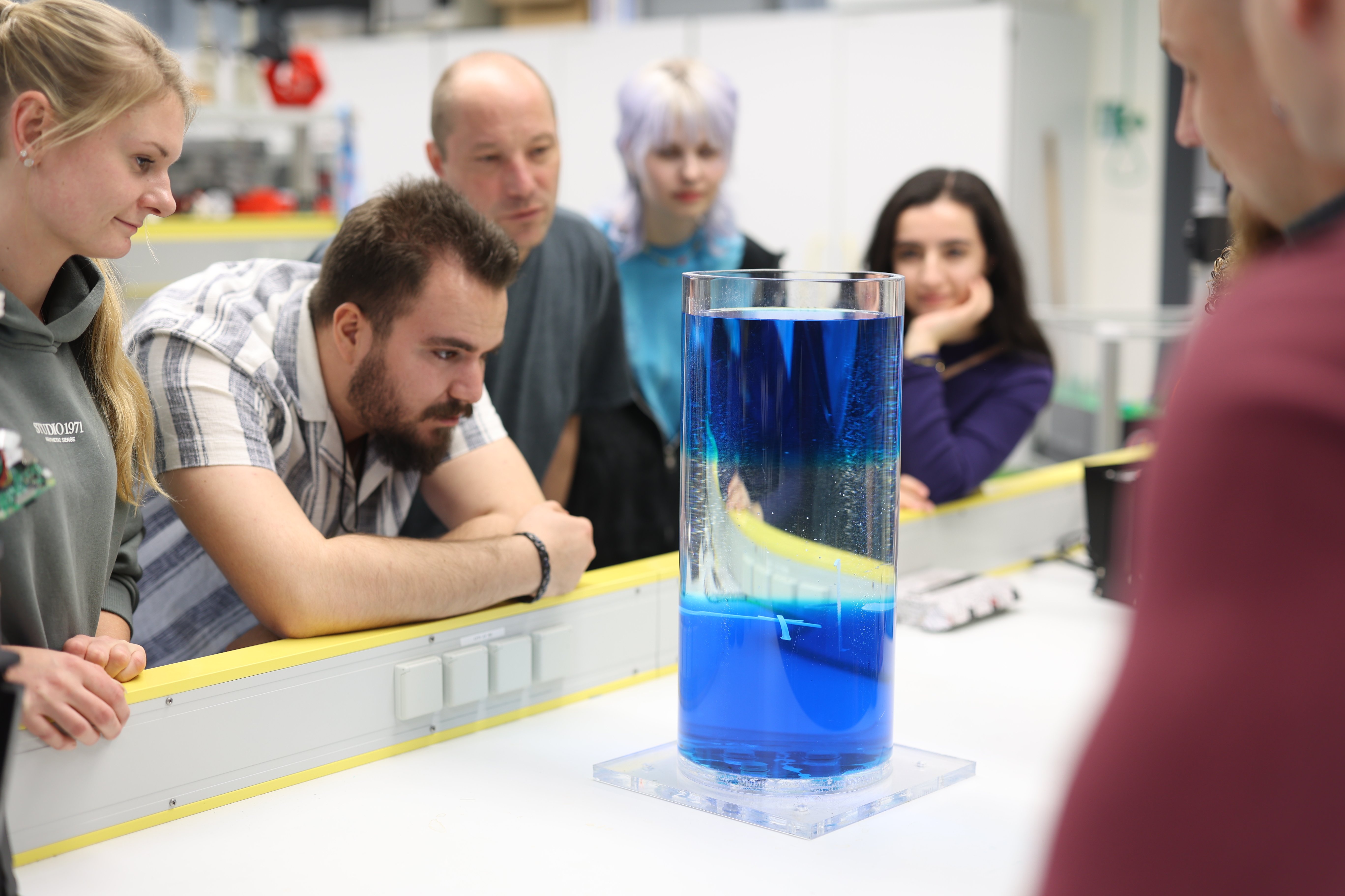 Studierende stehen mit dem Dozenten um eine Wassersäule herum und beobachten das Wasserverhalten.