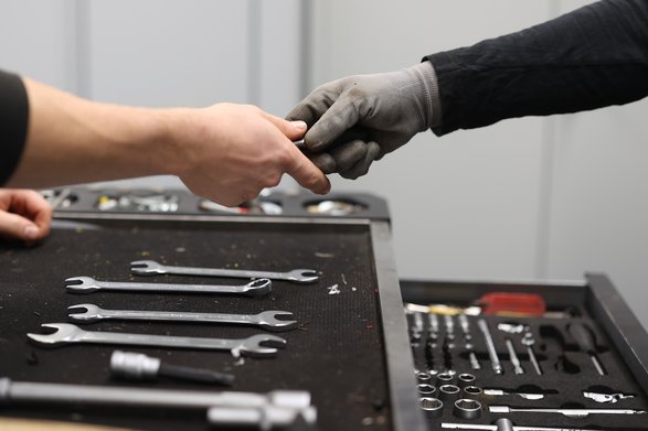 Zwei Hände am Werkzeugkoffer reichen sich etwas.