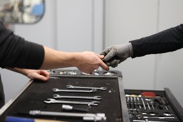 Zwei Hände am Werkzeugkoffer reichen sich etwas.