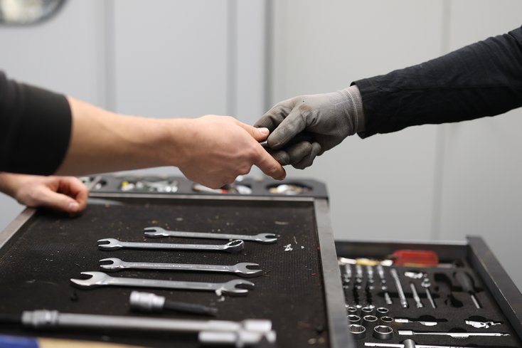 Zwei Hände am Werkzeugkoffer reichen sich etwas.