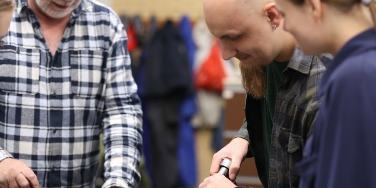 Ein Dozent erklärt Studierenden etwas an einem Motor.