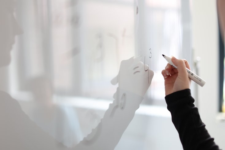 Person löst mathematische Gleichung am Whiteboard.