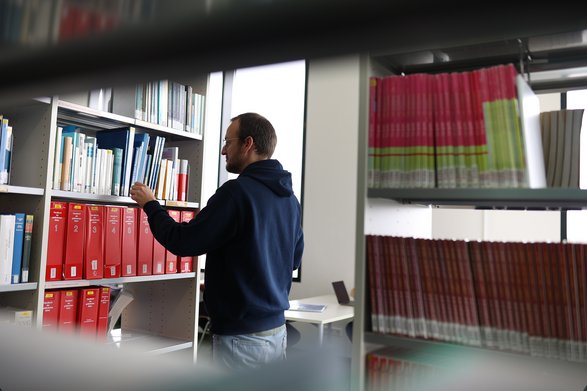 Student steht vor einem Regal in der Bibliothek