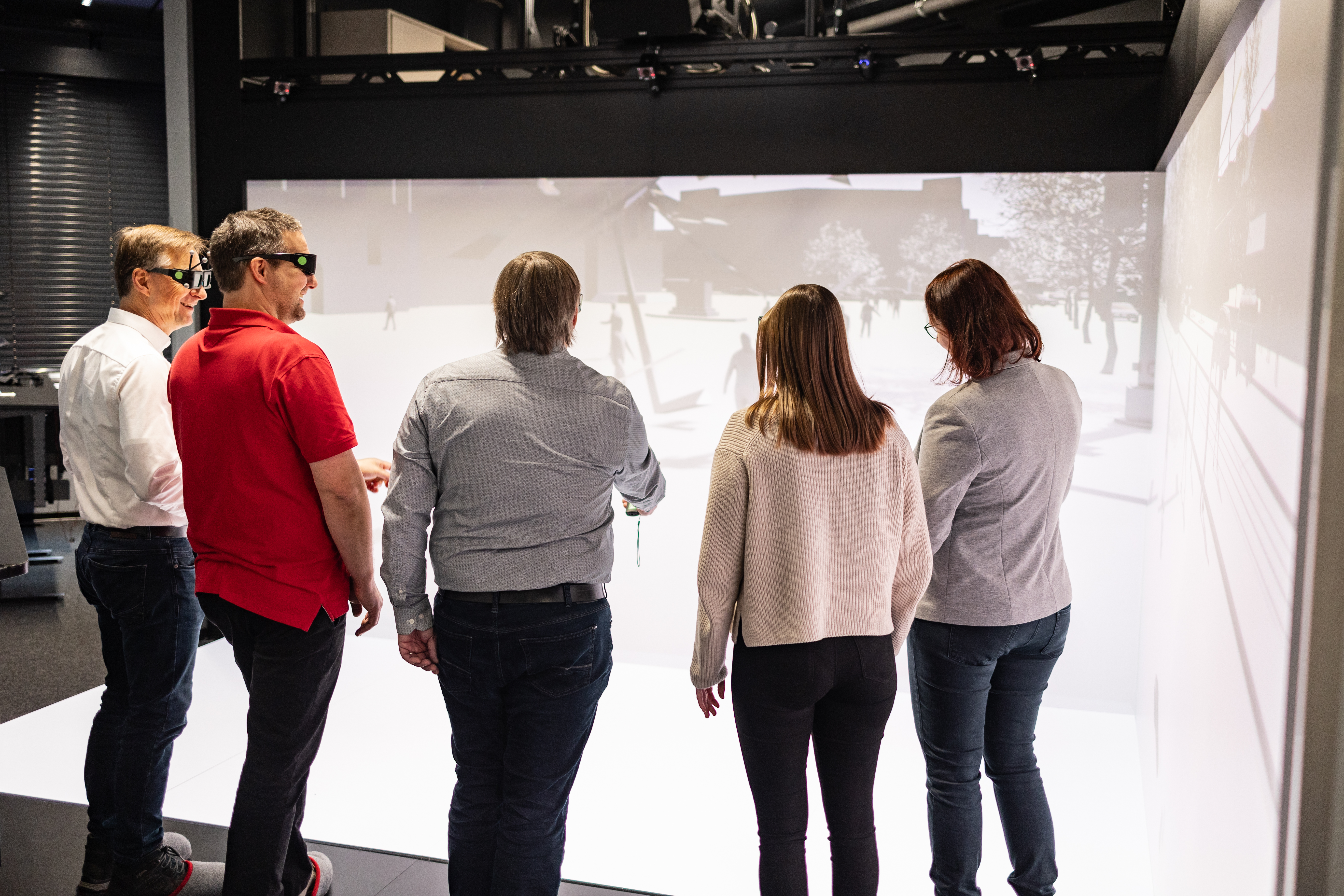 Männer und Frauen befinden sich in einem Virtual Reality Raum und diskutieren lächelnd.