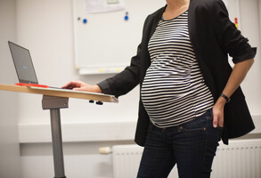 Schwangere Person an Stehtisch mit Laptop