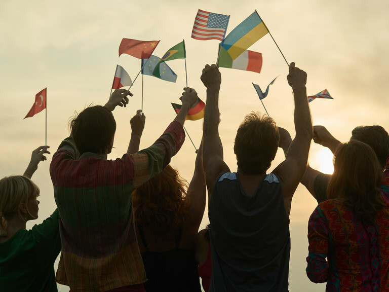 Silhouettes of people holding flags from various countries.