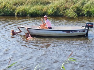 Eine Studierende sitzt im Boot, zwei Studierende schwimmen