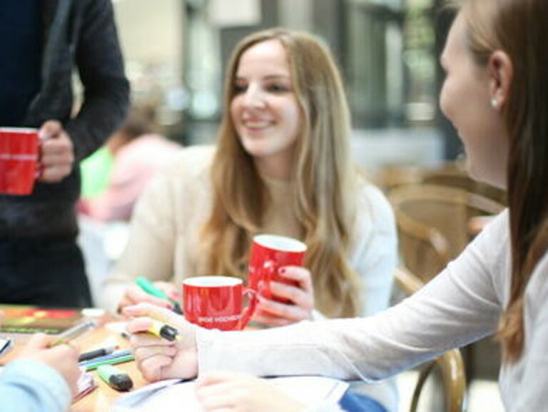 Students are sitting at a table with studying supplies and coffee mugs