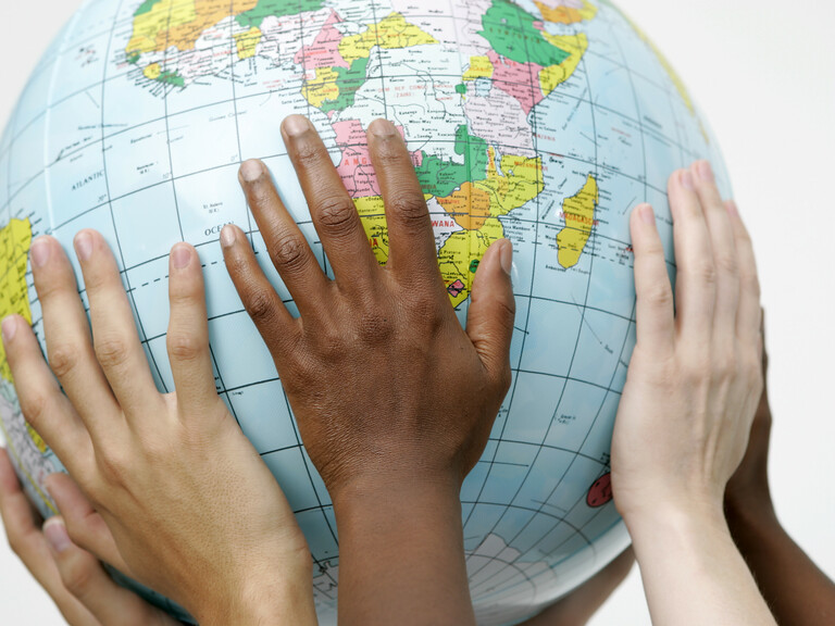 Hände verschiedener Hautfarben halten Globus in die Luft