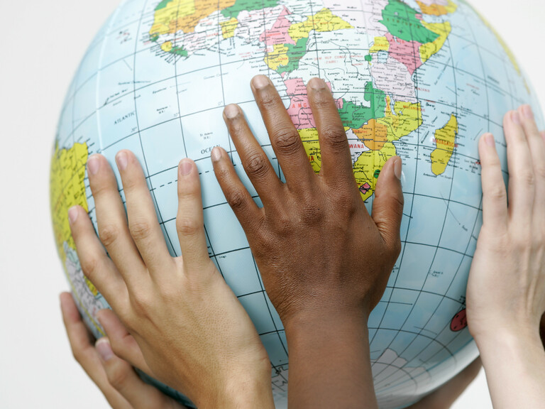 Hände verschiedener Hautfarben halten Globus in die Luft