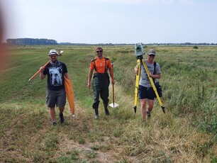 drei Studierende tragen Messgeräte über eine Wiese