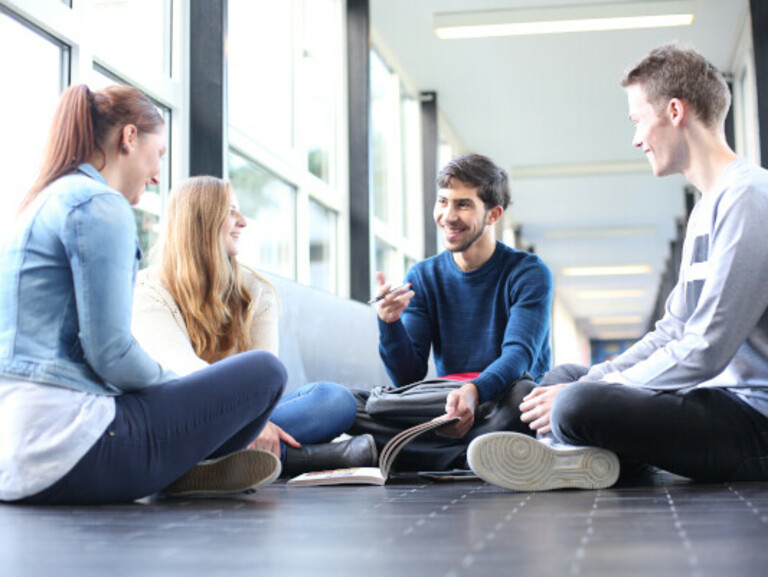 Group of students sitting in a circle on the floor of a hallway
