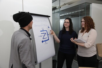 Drei Studierende brainstormen vor einem Roll-up