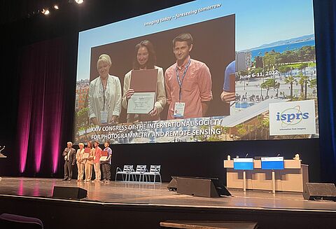 Preisverleihung beim ISPRS-Kongress in Nizza (v.l.): Dr. Julia Gorkovchuk, Dr. Maria Chizhova (mit Urkunde), Dr. Denys Gorkovchuk (auf der Leinwand)