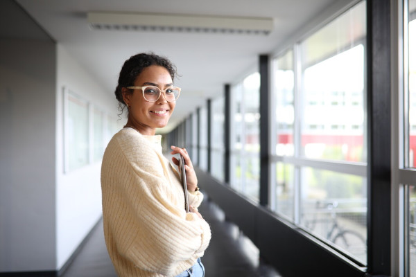 Studierende steht lächelnd im Flur des Hochschulgebäudes