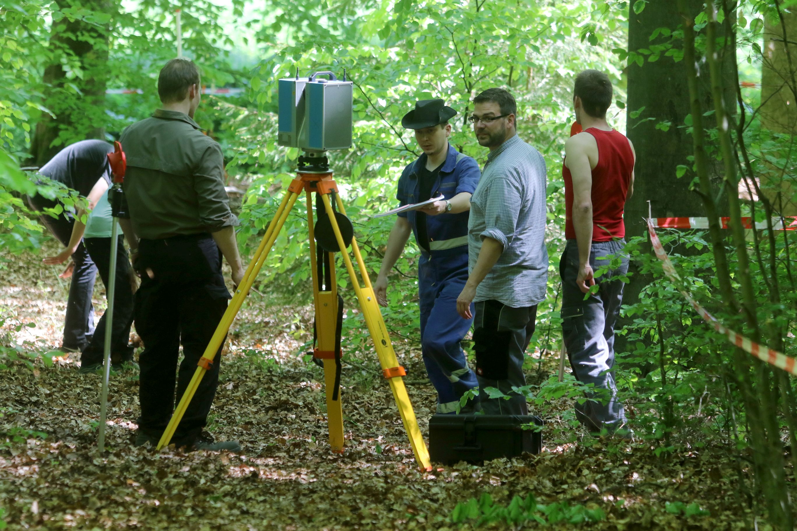 Mehrere Personen stehen im Wald um einen Laserscanner herum