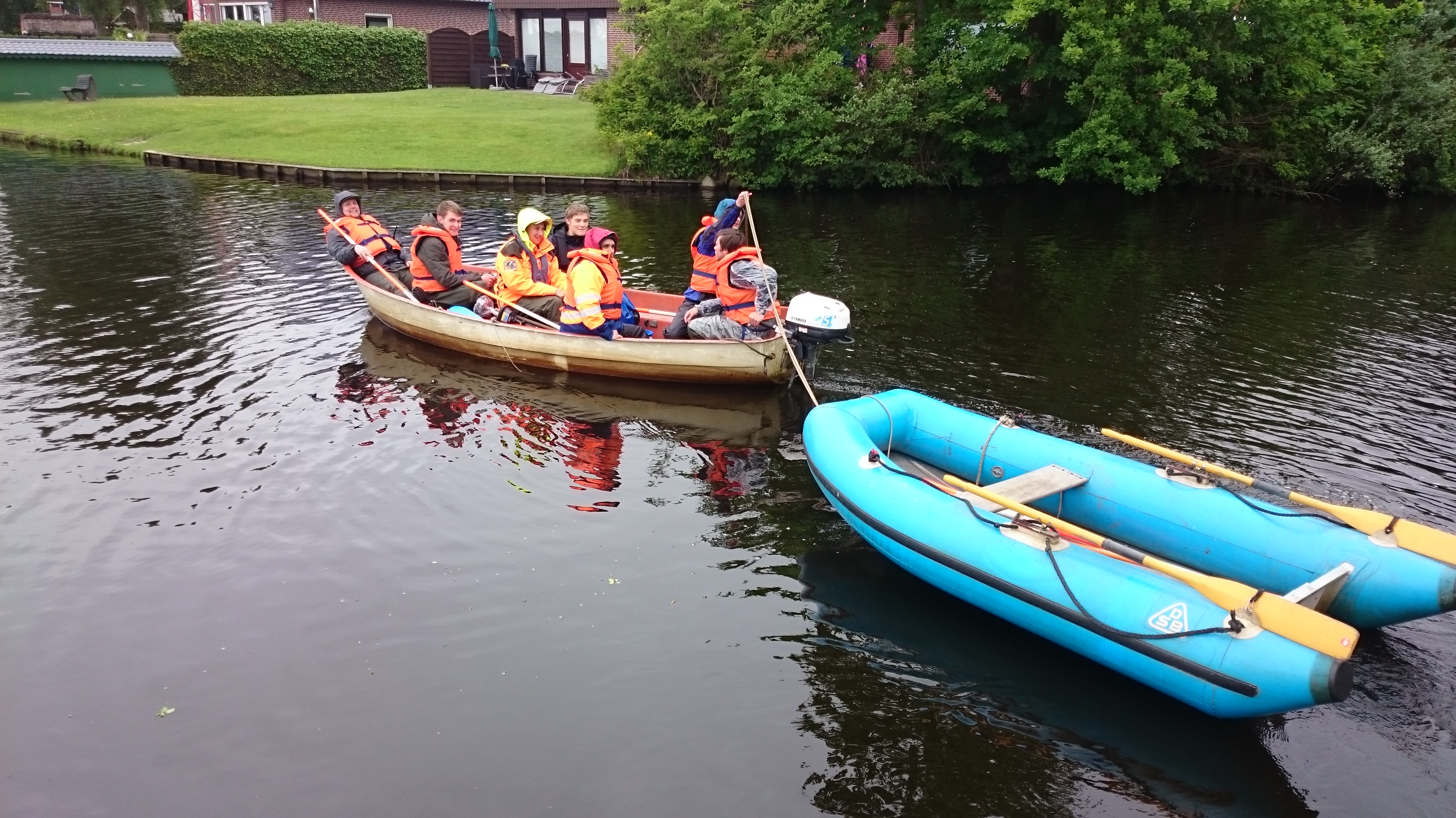 Mehrere Studierende sitzen in einem Boot mit Motor und ziehen mit Hilfe eines Seils ein Schlauchboot