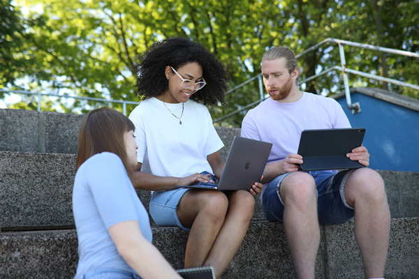 Drei Studierende auf der Treppe mit Laptop